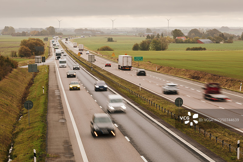 汽车和卡车在穿越农田景观的高速公路上行驶。图片素材