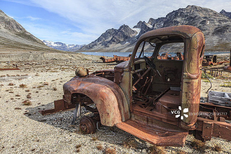 锈迹斑斑的汽车和油桶，背景是陡峭的山脉，二战时期美国空军基地的遗迹，伊卡泰克峡湾，格陵兰东部，格陵兰图片素材