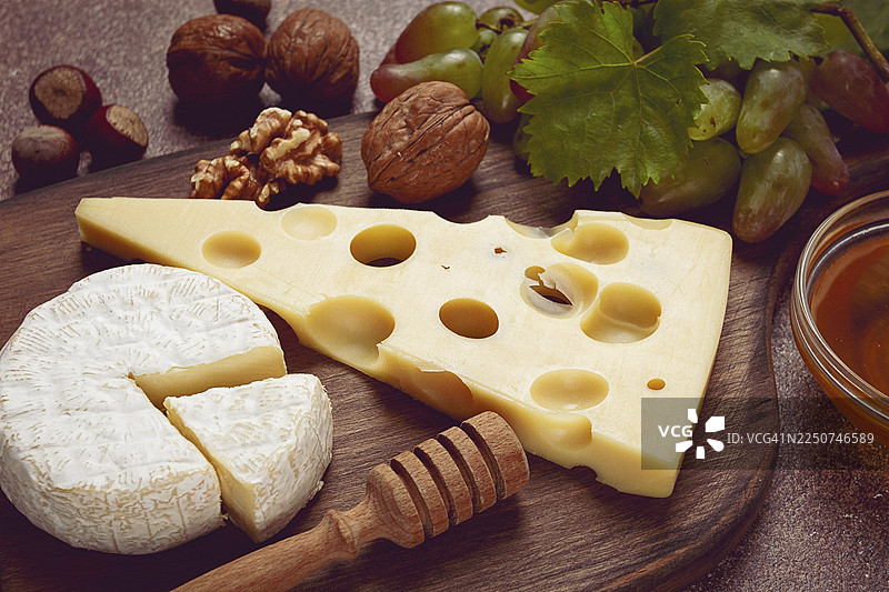 大孔奶酪，如埃门塔尔奶酪、马苏里奶酪、布里奶酪，放在砧板上，配有葡萄和蜂蜜、坚果，是搭配葡萄酒的开胃菜，俯视视角图片素材