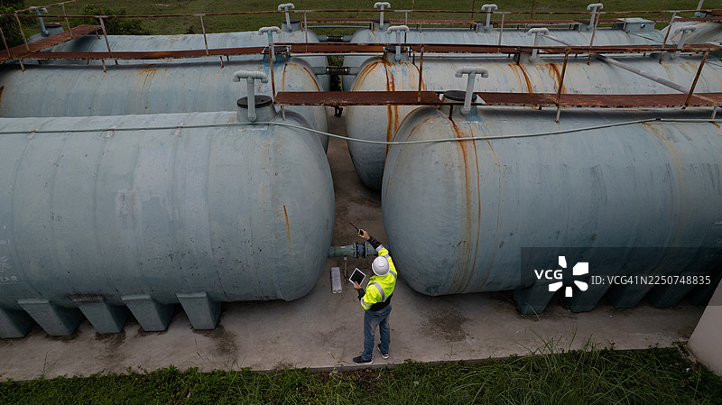 一名身穿荧光夹克的机械工程师在大型水箱之间进行维护服务的航拍图图片素材