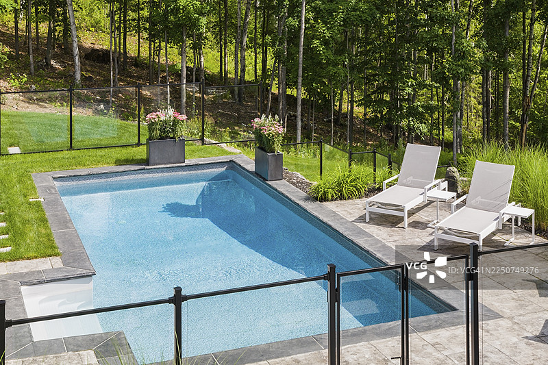 夏季，加拿大魁北克省，住宅后院，两张白色的长椅位于地下游泳池边缘，游泳池被透明玻璃和黑色金属栅栏环绕图片素材