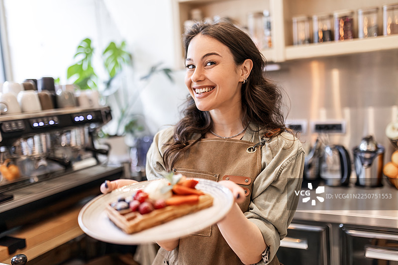 女顾客为自己盛上一盘撒满新鲜浆果的华夫饼图片素材