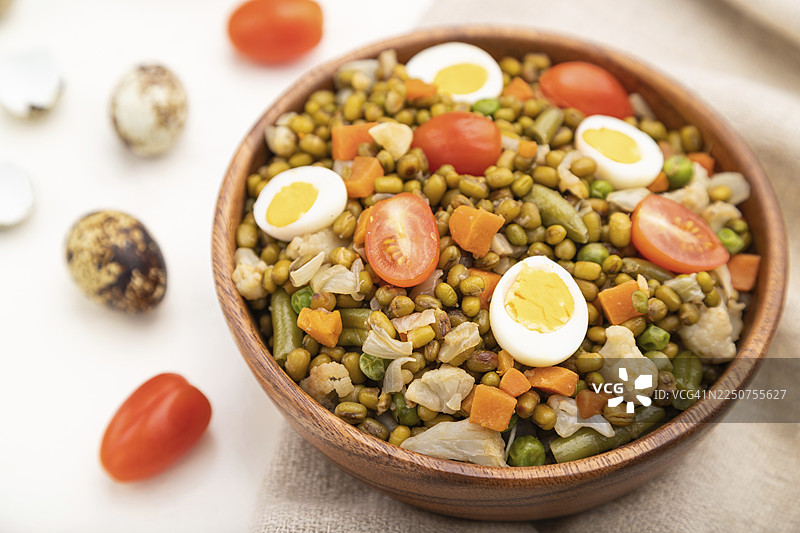 白木背景和亚麻布上的鹌鹑蛋绿豆粥、番茄和微型蔬菜苗。侧视图，特写，选择性聚焦图片素材