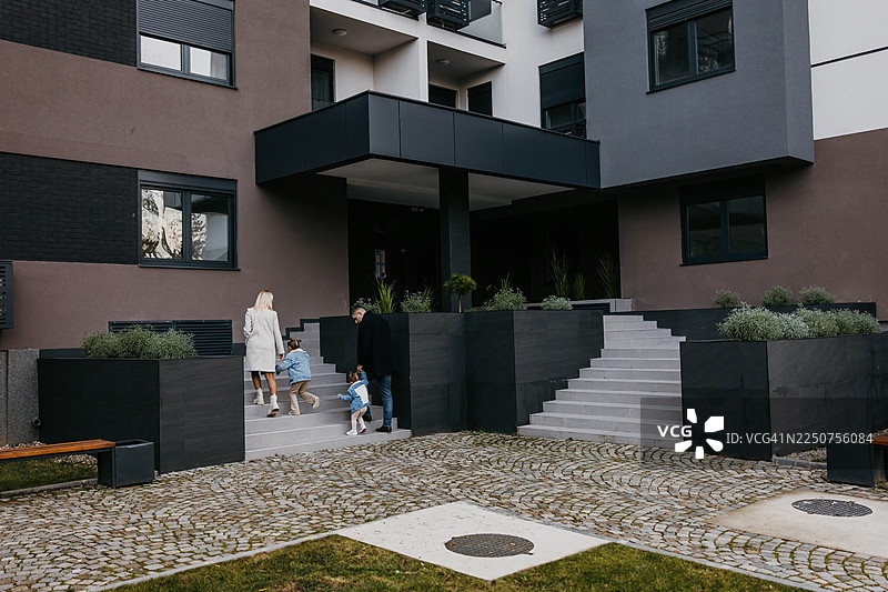 一家人在宁静的城市庭院入口处，走上现代公寓楼的台阶图片素材