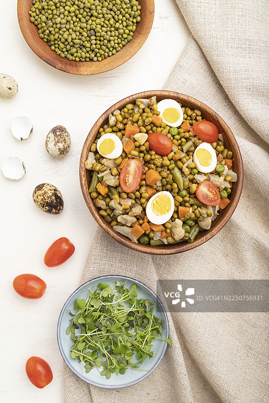 白木背景和亚麻织物上的绿豆粥，配以鹌鹑蛋、番茄和微型蔬菜嫩芽。俯视，平面布置，特写图片素材