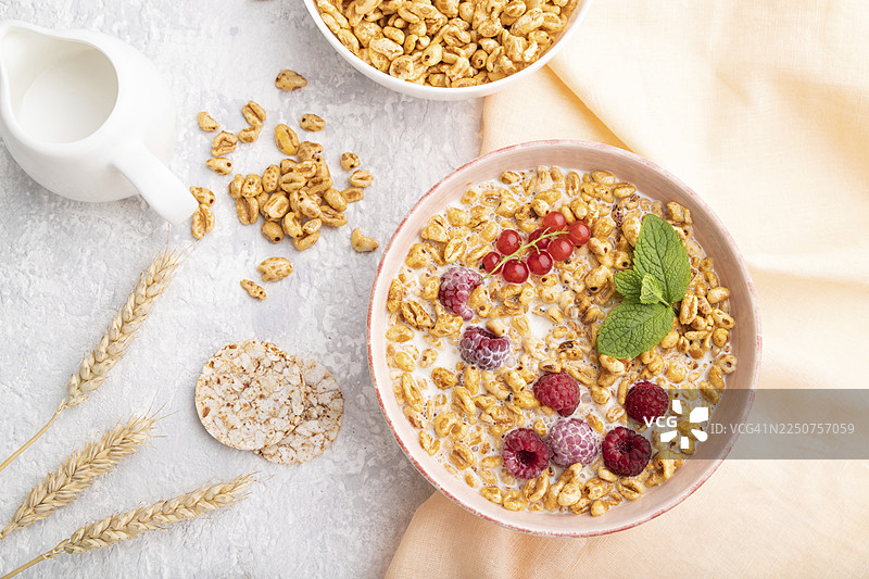 陶瓷碗中盛有牛奶麦片粥、覆盆子和醋栗，放在灰色混凝土背景和橙色亚麻布上。俯视，平铺，特写图片素材