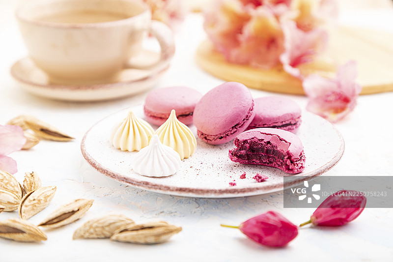 紫色的马卡龙或马卡龙蛋糕配咖啡杯，背景为白色混凝土，并用鲜花装饰。侧视图，特写，选择性焦点。图片素材