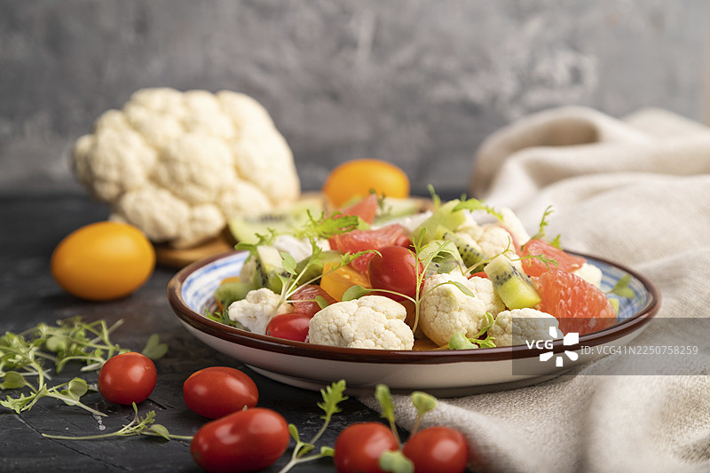 黑色混凝土背景和亚麻织物上的素食沙拉，包含菜花、卷心菜、猕猴桃、番茄、微型蔬菜苗。侧视图，特写，选择性聚焦图片素材