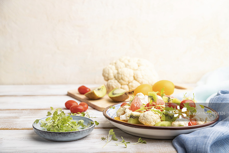 白色木质背景和蓝色亚麻织物上的素食沙拉，包含菜花、卷心菜、猕猴桃、番茄、微型蔬菜苗。侧面视图，留有复制空间，选择性聚焦图片素材