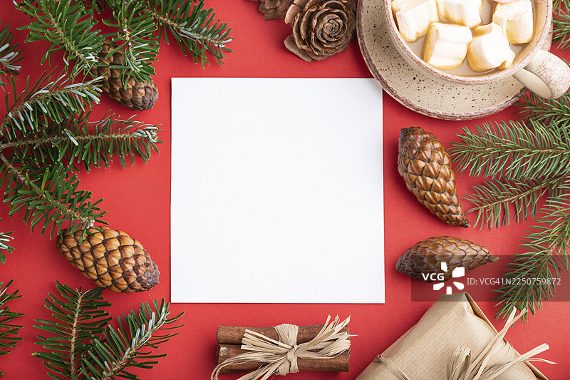 圣诞节或新年框架构图，模板。装饰品、盒子、肉桂、松果、冷杉和云杉枝、咖啡杯，放在红色纸张背景上。俯视，留白，平面布置图片素材