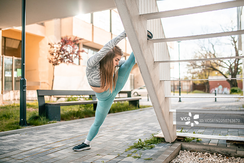 年轻的女舞者在开始锻炼前伸展身体，将一条直腿放在楼梯上，高举过头顶图片素材
