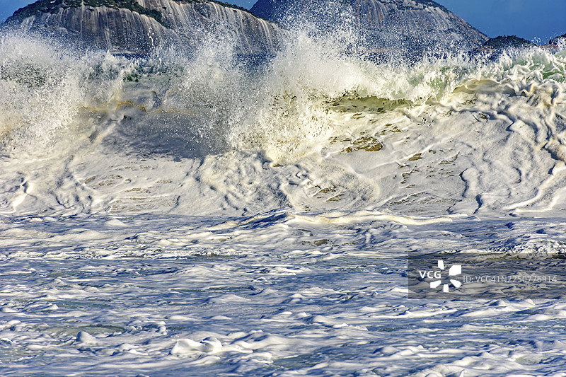 阳光明媚的日子里，巴西海滩上出现了一道美丽而强劲的海浪，水珠和泡沫在空中飞溅。图片素材