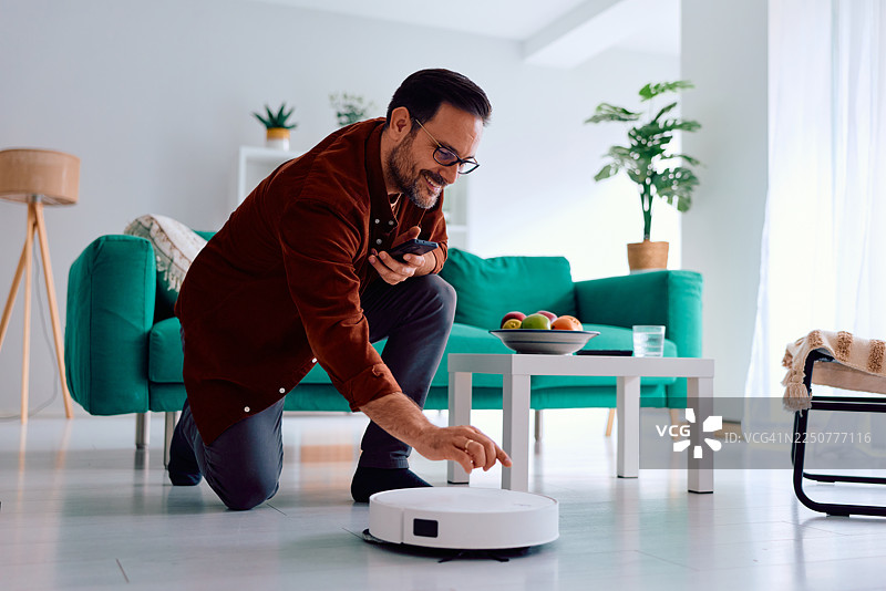 客厅里，一名成年男子正在启动智能扫地机器人图片素材