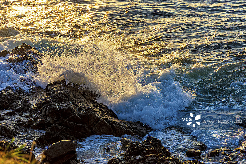 夕阳下的巴西萨尔瓦多城，海浪拍打岩石激起水花和浪花飞溅图片素材