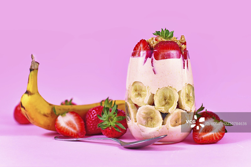 新鲜食材环绕，玻璃杯中盛放着酸奶和格兰诺拉麦片分层叠放的夏日健康香蕉草莓水果甜点图片素材