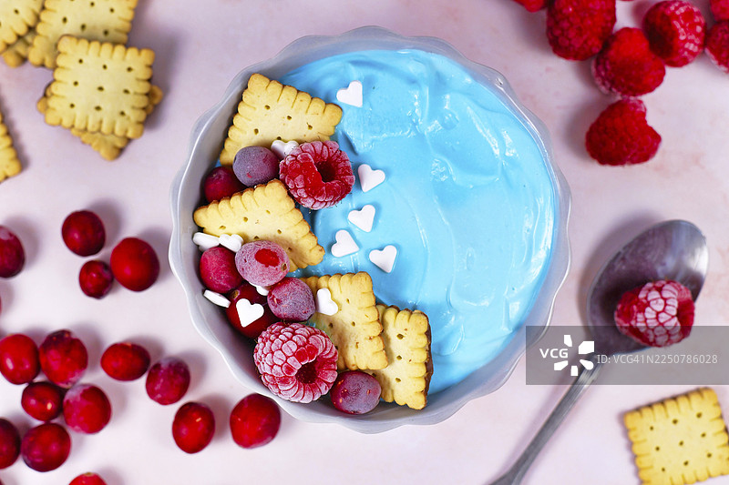 健康的酸奶水果思慕雪碗，加入天然蓝色螺旋藻粉，顶部装饰有红色覆盆子、蔓越莓和几块小饼干。图片素材