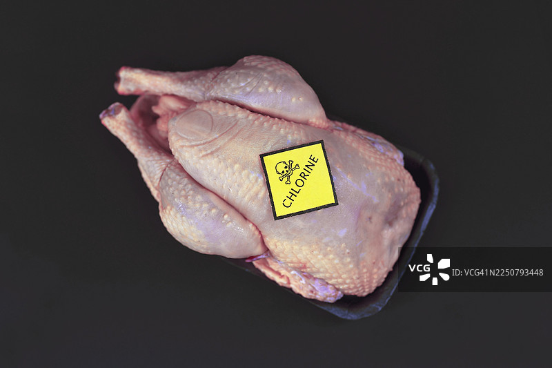 氯化鸡肉概念图，一只生鸡胸肉，上面贴有带有骷髅标志和“Chlorine”字样的黄色警告标签，背景为黑色图片素材