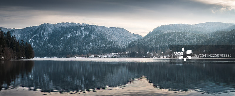 冬季白天，从湖岸远眺隆日梅湖的全景，可以看到沃日斯山脉的雪岭和针叶林倒映在平静的湖水中，地点为法国东部洛林地区肖鲁普-隆日梅。图片素材