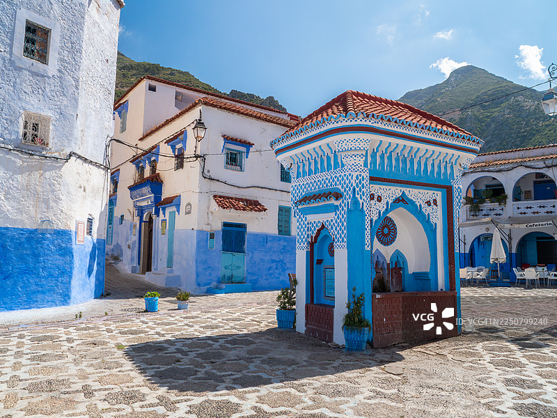 摩洛哥丹吉尔-德托万-胡塞马地区舍夫沙万市麦地那哈乌塔鹅卵石广场的阿拉伯风格饮水喷泉的广角视图,那里有著名的“蓝色之城”,还有蓝白相间的建筑和装饰性的盆栽植物。图片素材