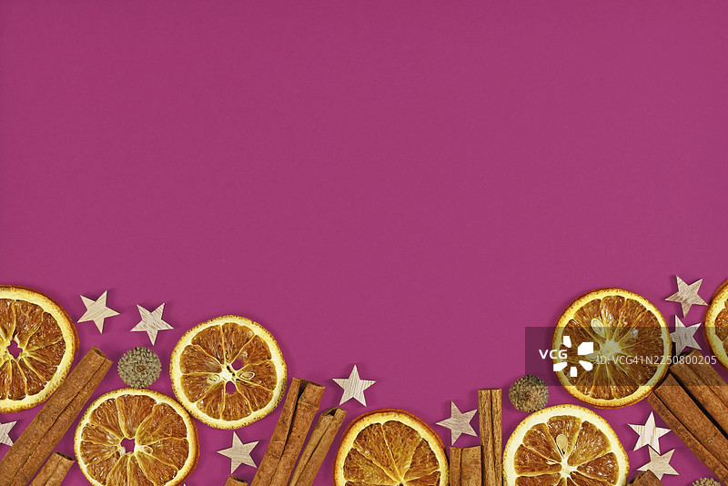 粉色背景底部，带有季节感的平铺构图，包含天然干橙片、肉桂棒和星星装饰，留有空白复制空间图片素材