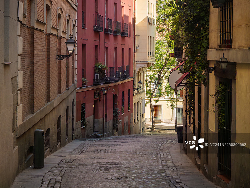 马德里拉拉蒂纳区，早晨，一条狭窄的鹅卵石下坡路，两旁是色彩缤纷的住宅楼和公寓，马德里自治区 - 西班牙。图片素材