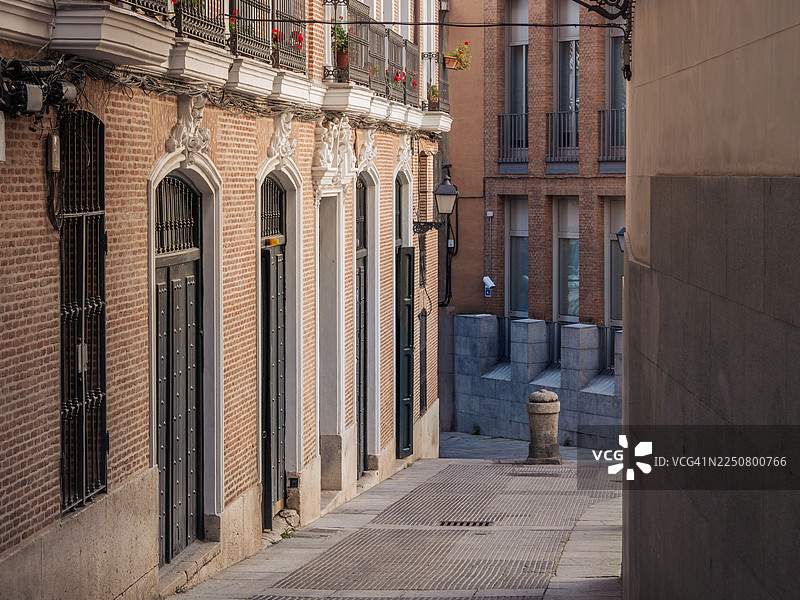 马德里市中心和帕拉西奥区的一条狭窄下坡街道的特写镜头，街道两旁是办公楼、住宅楼和带大窗户及砖墙的公寓，拍摄于西班牙马德里自治区的一个早晨。图片素材