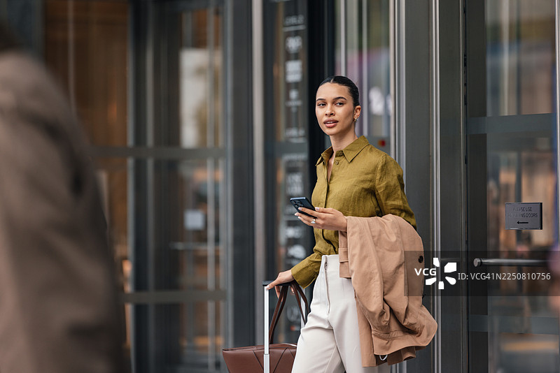 女商人在街头，将外套搭在手臂上，正走进办公楼图片素材
