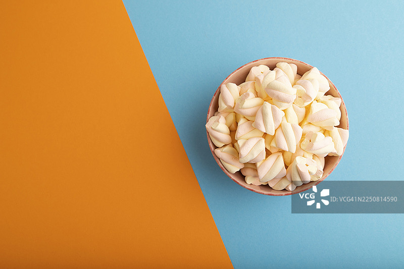 陶瓷碗里的橙色和粉色棉花糖，背景为蓝橙色柔和纸张，俯视，平铺，留白，极简主义图片素材