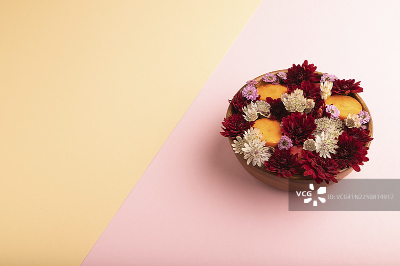 木碗盛着胡萝卜片和红色雏菊、山踯躅，花卉沙拉，背景为粉橙色柔和纸张，侧面视角，留有复制空间，极简风格图片素材