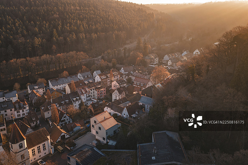 在金色天空下，森林边缘的村庄笼罩在温暖的光线中，德国普福尔茨海姆的迪尔维森施泰因图片素材