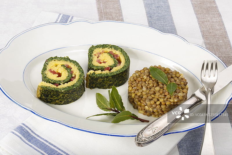 德国南部菜肴，玉米糊菠菜卷配阿尔布雷希特扁豆，盛放在餐盘上，配有月桂叶、扁豆蔬菜、熏肉、培根丁，健康，美食摄影，影棚，德国图片素材