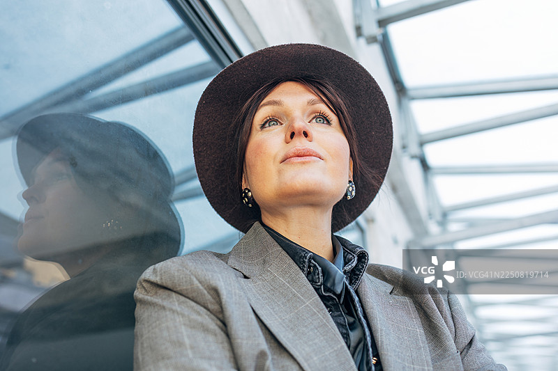 戴着帽子的女人抬头望向窗户，窗户上映出了她的倒影图片素材