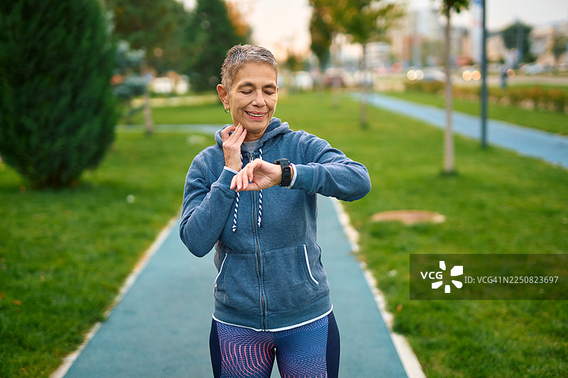一位年长女性在慢跑锻炼时，查看自己的脉搏和智能手表图片素材