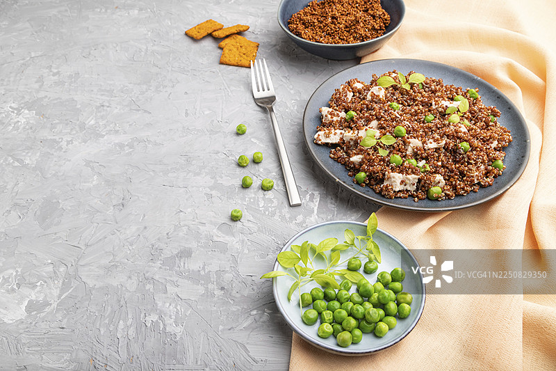 陶瓷盘中的藜麦粥，配有青豆和鸡肉，置于灰色混凝土背景和橙色纺织品上。侧视图，特写，留有复制空间图片素材