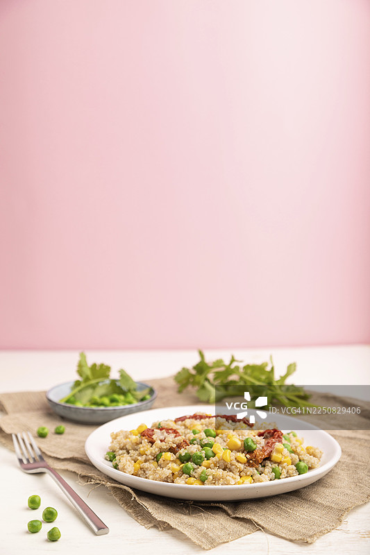 白色和粉彩粉色背景上的陶瓷盘子里的藜麦粥，配有青豆、玉米和干番茄，以及亚麻布。侧视图，留有复制空间。图片素材