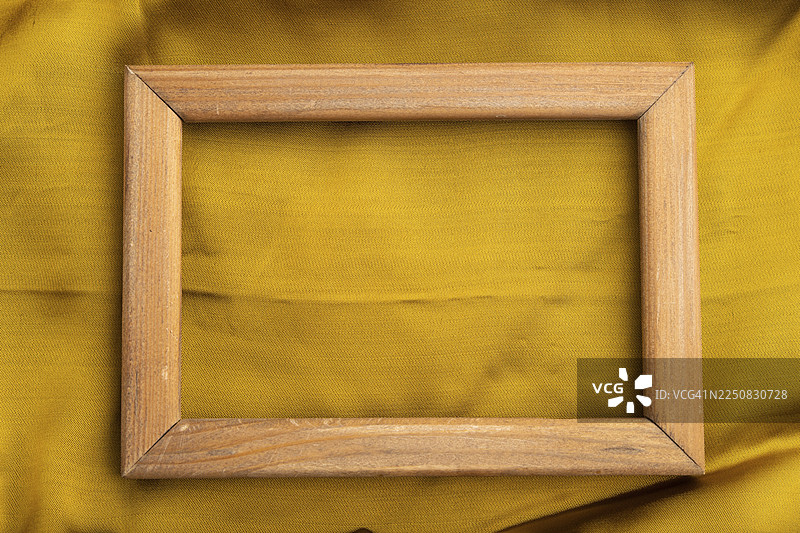 光滑的黄色丝绸纸上的木制框架。俯视，平铺，天然纺织品背景和纹理图片素材
