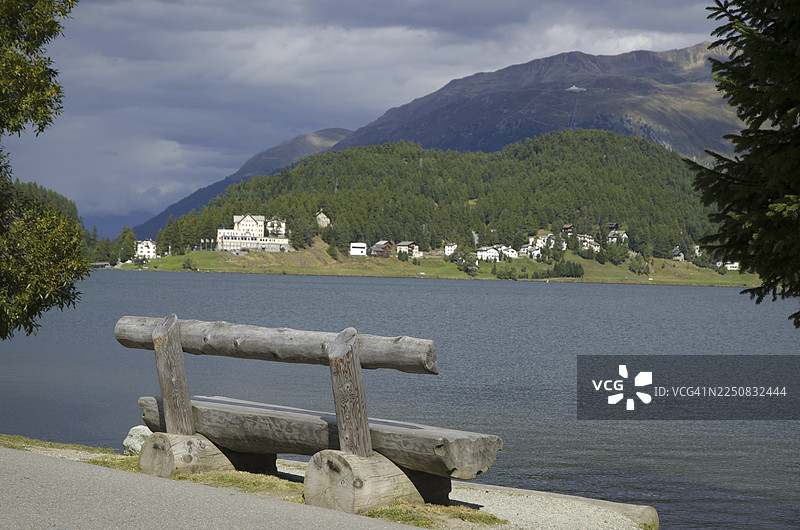 瑞士晴天，圣莫里茨湖畔的长椅与树木，背景是远山和灰色的云彩图片素材