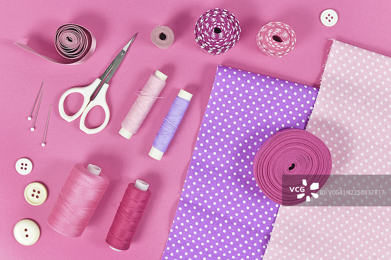 粉色背景上各种缝纫工具的平面图，包括布料、剪刀、线轴、纽扣或图钉图片素材