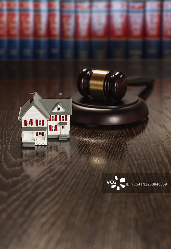 木桌上放着法槌和微缩房屋模型，背景是法律书籍。图片素材