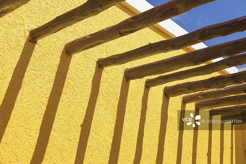抽象的木柱梁与蓝天下的明亮黄墙图片素材
