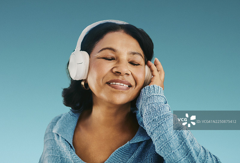 一位成熟的女性戴着耳机在蓝色背景下享受放松的健康时光，聆听音乐图片素材