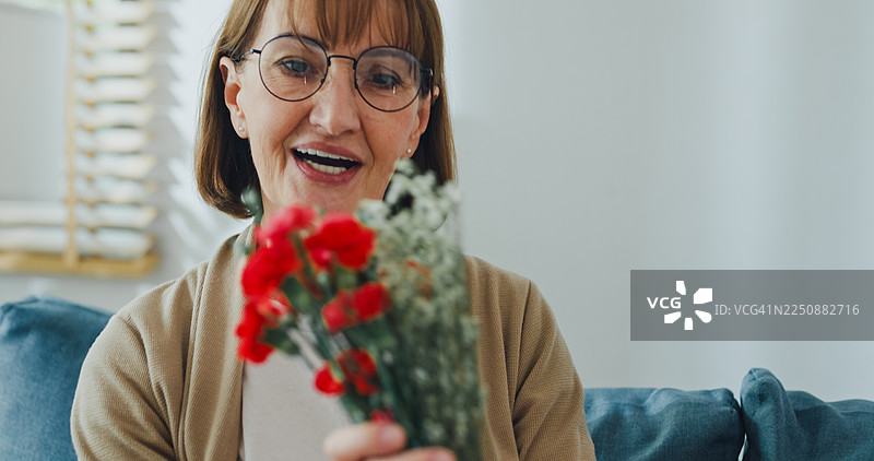 在一个客厅的沙发上，十几岁的白人儿子把一束花送给惊讶的母亲。家庭生活方式和母亲节概念。图片素材