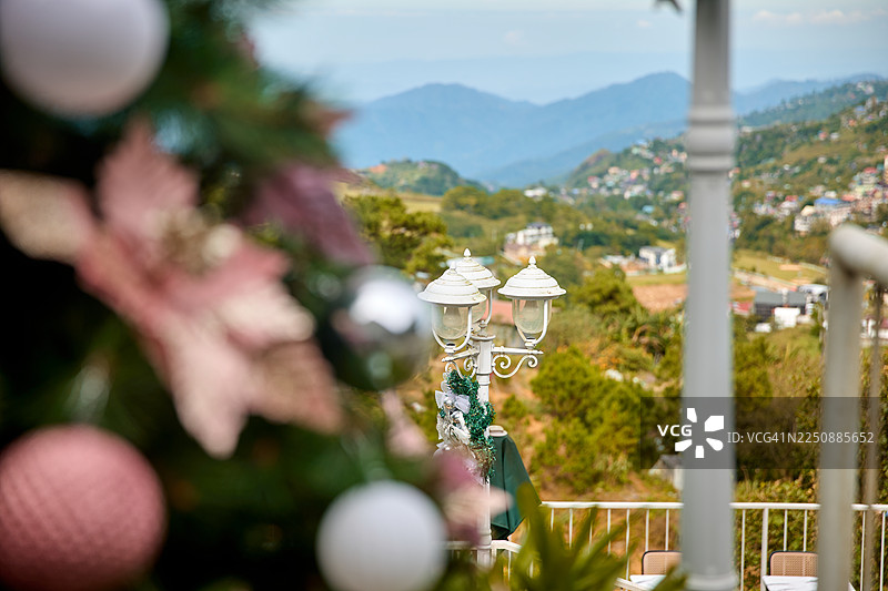 一棵装饰精美的圣诞树在前景中，中间有一个白色灯柱。图片素材