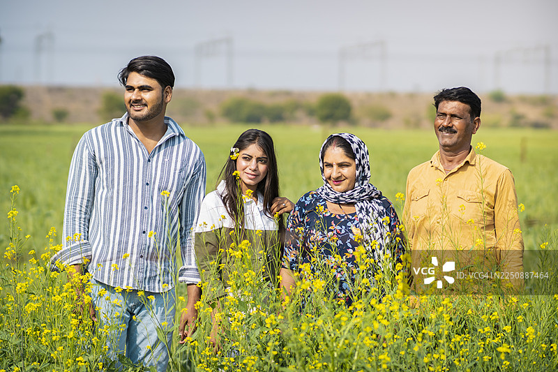 快乐的印度家庭站在芥末农田里。图片素材