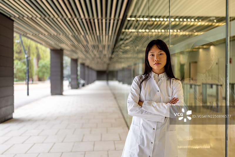 身穿白色实验服的专业女科学家自信地站在现代玻璃走廊里图片素材
