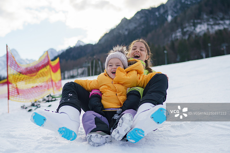 快乐的姐妹俩在雪山坡上一起玩耍。图片素材