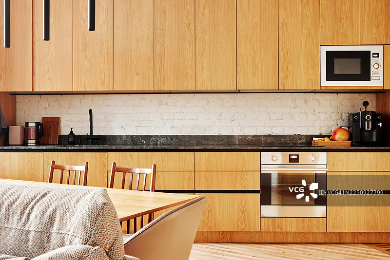 温馨的现代厨房，配有温暖的木制橱柜、不锈钢烤箱和休闲餐桌图片素材