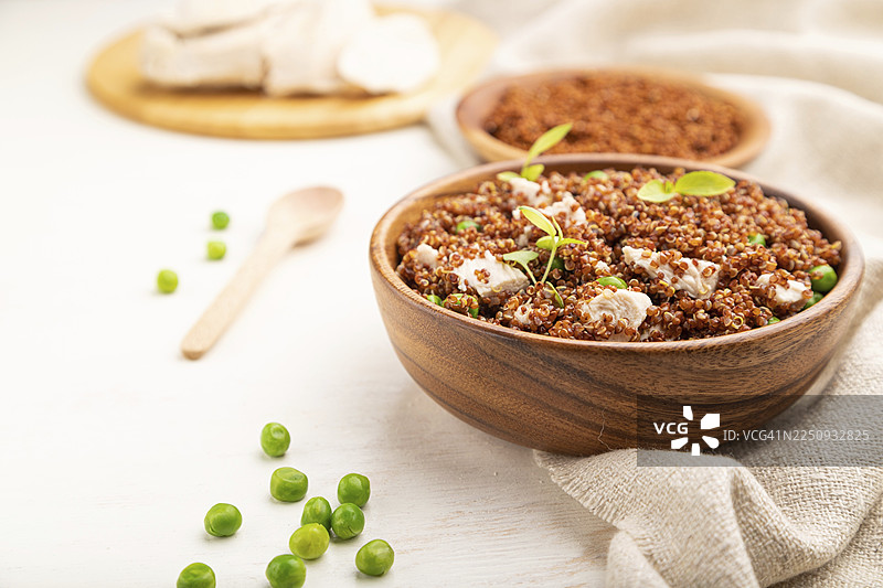 白色木质背景和亚麻纺织品上，木碗里盛着藜麦粥，配有青豆和鸡肉。俯视，特写，选择性对焦图片素材