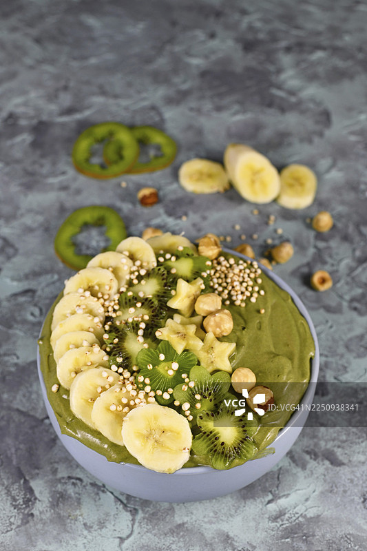 灰底上放着绿色水果思慕雪碗，上面点缀着星星形状的香蕉、猕猴桃、榛子和膨化藜麦谷物图片素材