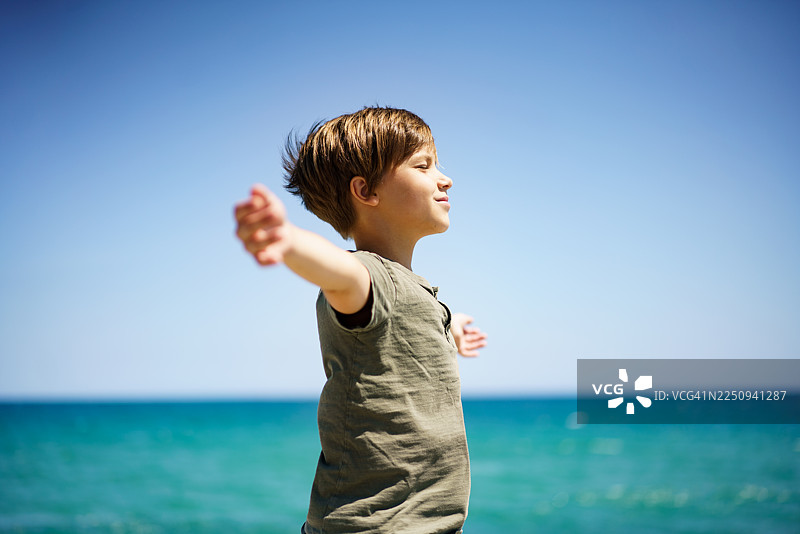 少年敞开双臂，在海边感受自由。图片素材